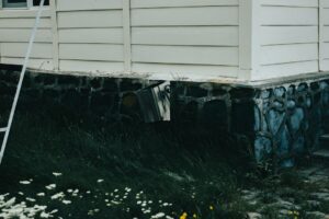 Homeowner examining a basement foundation wall with a flashlight and measuring a crack.